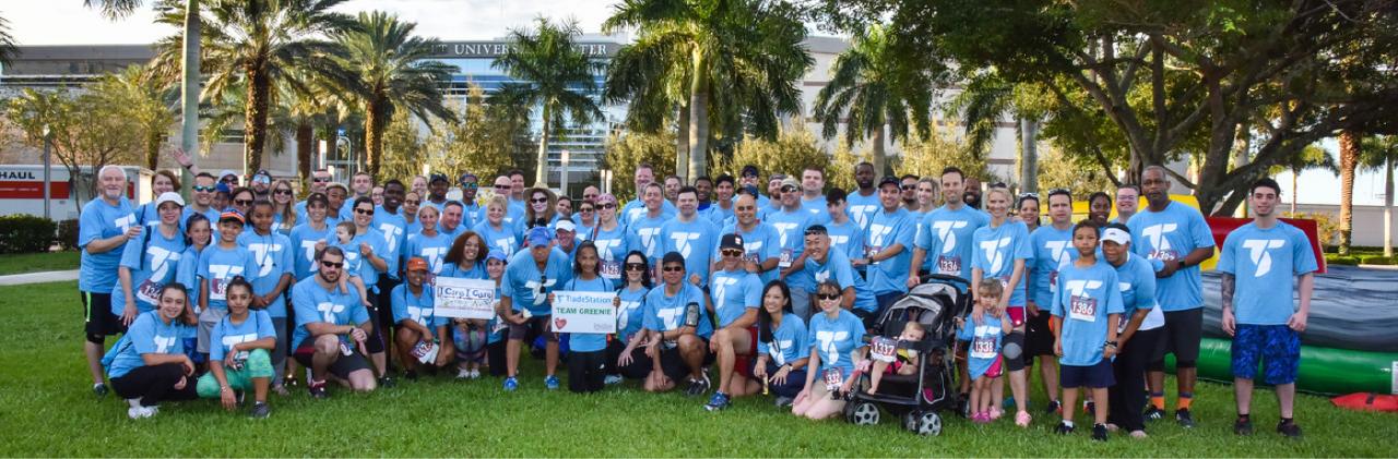 A group photo of about 80 TradeStation members and their families wearing the corporate T-shirt.
