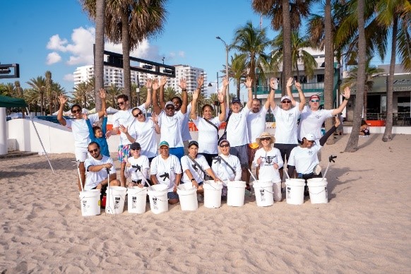 Photo of employees and their families wearing corporate T-shirts cleaning up along the beach.